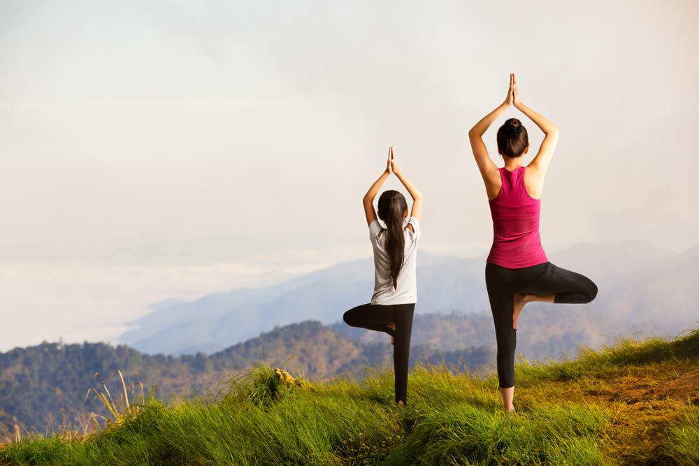 Mother and daughter doing yoga at top of mountain
